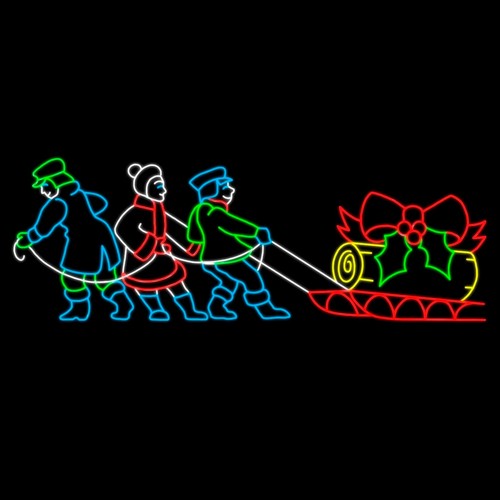 Brightly lit silhouette of three children pulling a red sled with a Yule log in yellow LED lights, adorned with a big red bow and green holly. The children are in Victorian dress, depicted in vibrant, green, white, blue and red LED lights against a black background, creating a festive and cheerful holiday display.