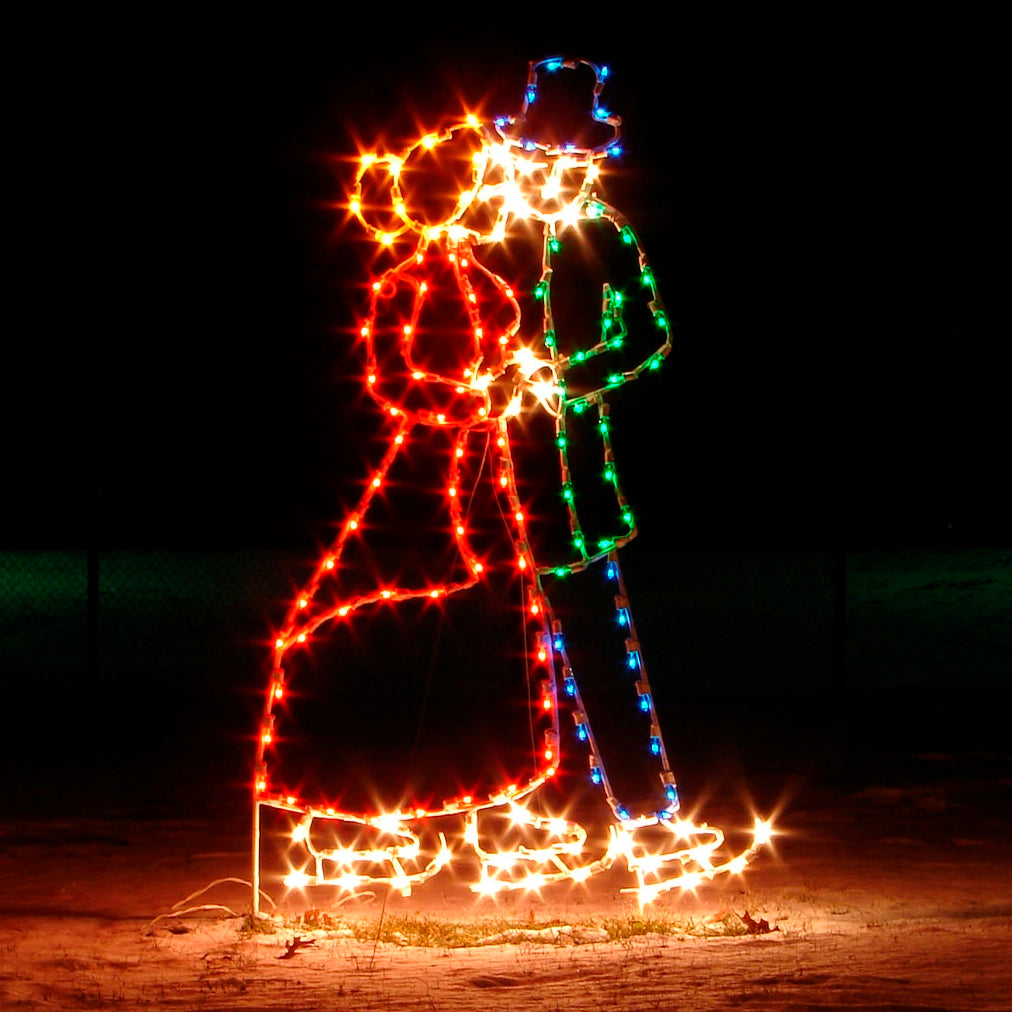 An enchanting silhouette depicting a couple ice skating, intricately illuminated with vibrant red, white, blue, and green LED lights. The couple is dressed in Victorian dress, with the woman in a red coat and the man in a green coat and flat top hat, creating a festive and romantic scene. The lights shine brightly against the dark background, highlighting the graceful movement of the skaters and adding a magical touch to holiday events.