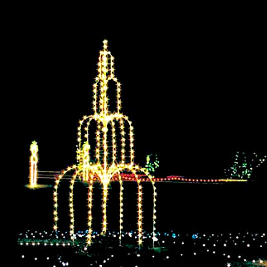 A vibrant animated fountain silhouette LED display shines brightly against a dark night sky. The fountain is outlined in warm white LED lights, creating a cascading water effect that draws attention and adds holiday cheer. In the background, additional holiday lights and decorations enhance the overall enchanting scene.