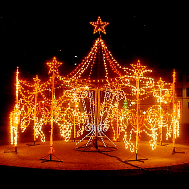 A dazzling LED silhouette display of a carousel with horses, intricately outlined in bright golden lights. The carousel features multiple star-topped poles and LED string lights creating a canopy effect, with detailed horse figures and horse reins in golden LED lights arranged in a circle, all set against a dark night background.