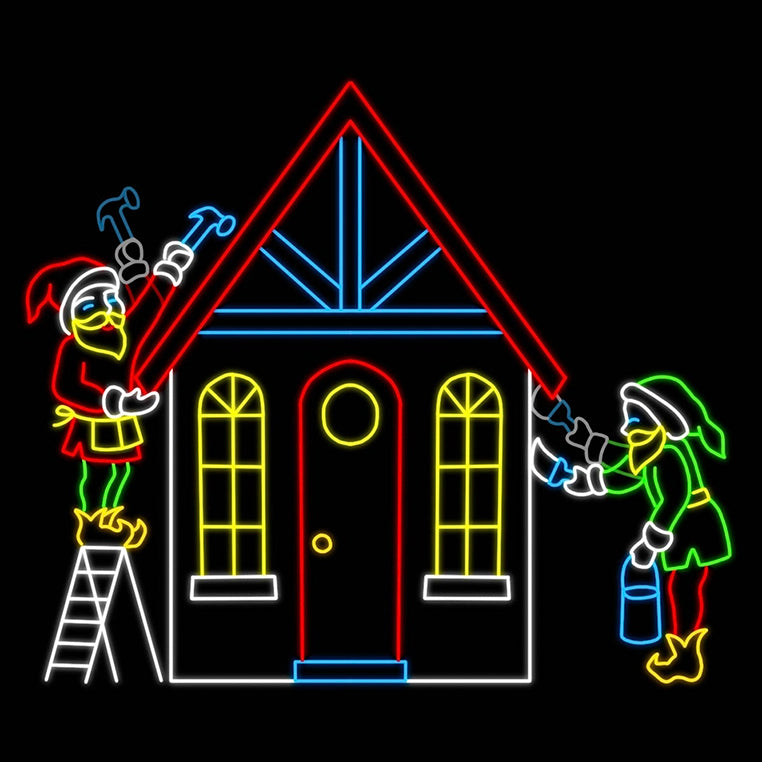 A vibrant LED silhouette display depicting two Christmas elves building a cozy cottage. One elf, dressed in green and red with a red Santa hat, stands on a ladder holding a hammer, while another elf with a green Santa hat paints the house. The house itself is outlined in colorful lights, featuring a red roof and bright windows, creating a festive scene against a black background.