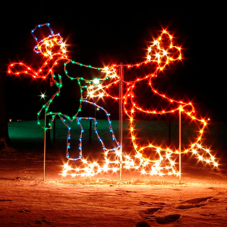 A silhouette LED display of a couple, in Victorian dress, dancing on ice skates, with the man wearing a flat top hat and the woman wearing a bonnet, outlined with bright white, green, blue, and red lights, set against a dark background.