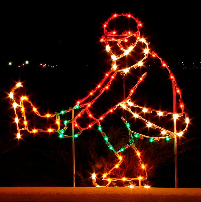A silhouette LED display of an ice skater, in Victorian dress performing a sit spin, outlined with bright red, green, and white LED lights, set against a dark background.