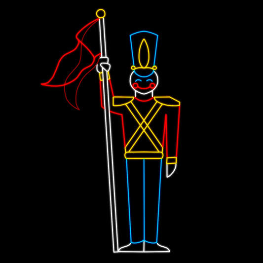 An animated silhouette LED display of a toy soldier holding a staff with a flag. The soldier is dressed in a colorful uniform with a tall blue hat, red jacket, yellow accents, and blue pants. The display is outlined with bright red, yellow, white, and blue LED lights, set against a black background.